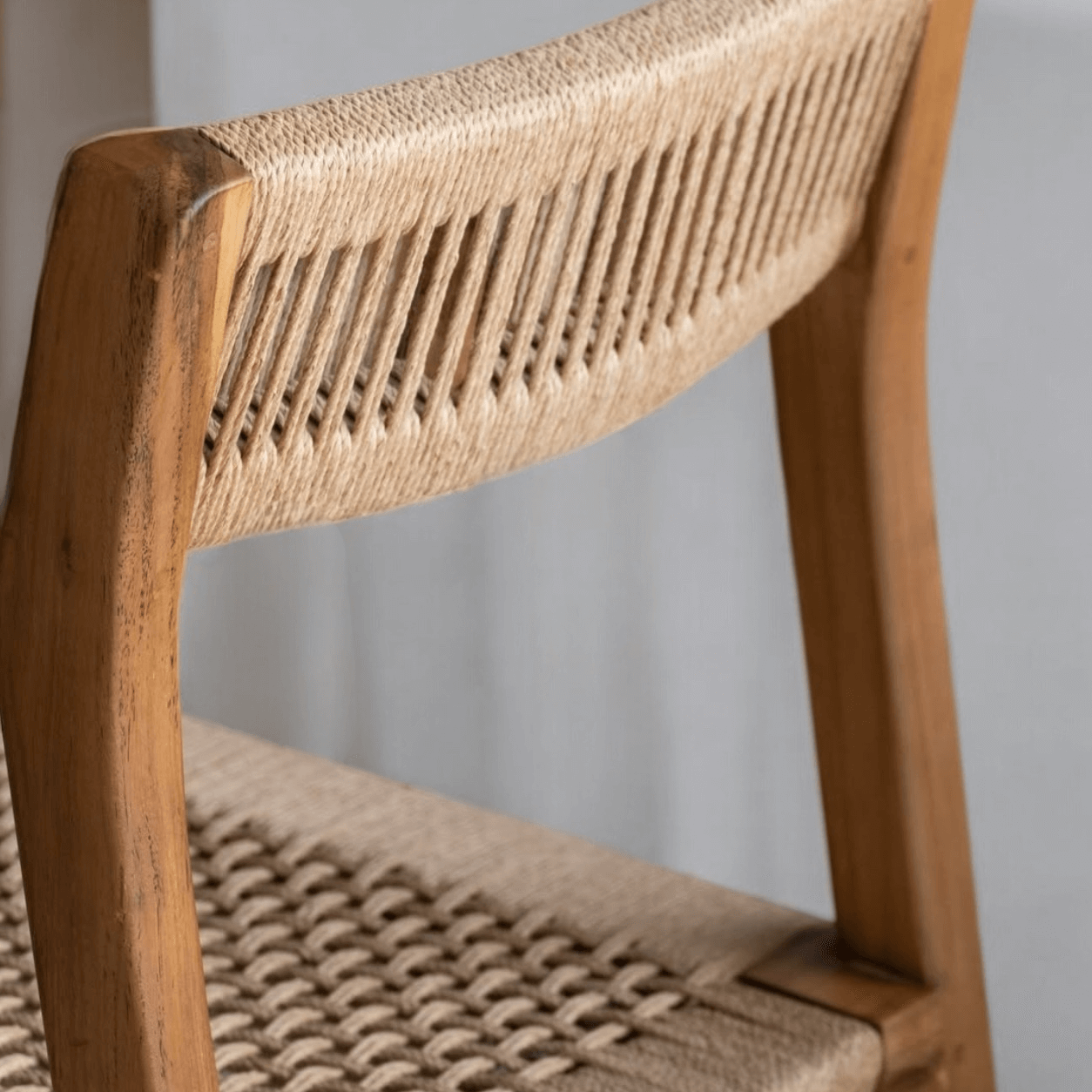 Close-up of a teak dining chair showcasing the handwoven natural loom backrest and seat detailing.